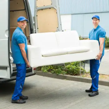 Zwei Männer in blauer Arbeitskleidung tragen ein weißes Sofa zu einem Transporter